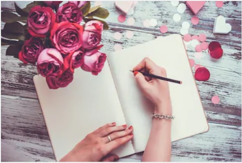 خاتون نوٹ بک پر لکھتے ہوئے اور پھولوں کا گل دستہ