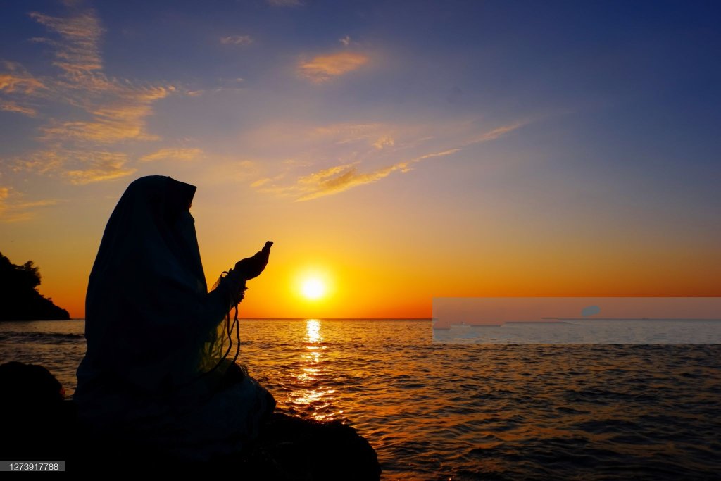 ایک مسلمان خاتون دعا مانگ رہی ہے، سمندر کنارے جبکہ سورج ڈوب رہا ہے
