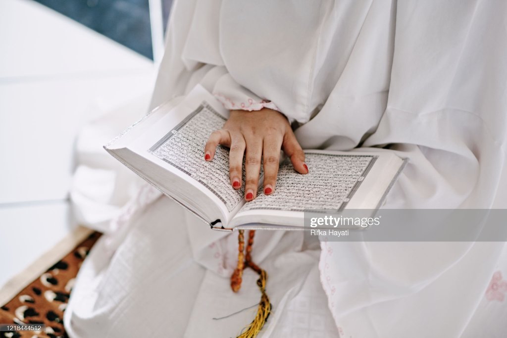 سفید لباس میں مسلمان خاتون قرآن مجید کی تلاوت کرتے ہوئے
