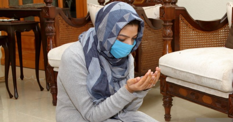 ماسک اور سکارف پہنے مسلمان خاتون دعا مانگ رہی ہے
