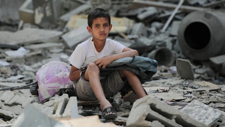 فلسطینی لڑکا اپنے تباہ شدہ گھر کے ملبے پر بیٹھا ہے